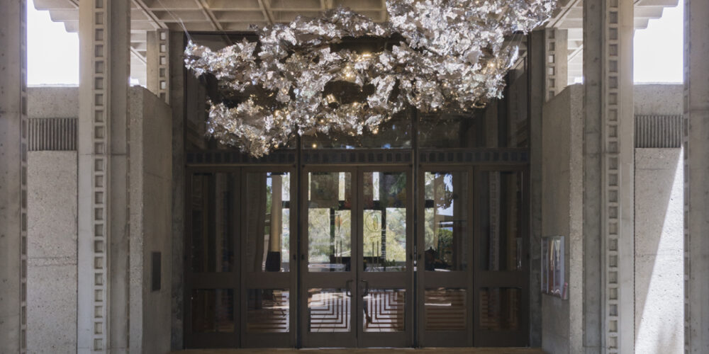 This is an artwork by the artist Olga Lah featuring silver, reflective material in a cloud-like shape hanging above the gallery's entrance doors outside.