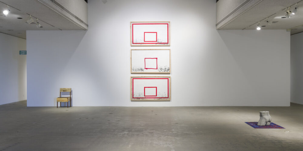 In this artwork installation by the artist David Alekhuogie, one artwork is a wooden sculpture of a low-sitting chair with rectangular, blocky shapes. To the right of this work, are three, vertically hanging artworks that resemble basketball backboards. In these works, there are various numbers of black handprints towards the bottom edge of the artworks. The background for these works is white with red outlines for the frame and rim. To the right of these works is a concrete, naked bust of a male mannequin figure. This artwork is placed on top of another artwork that depicts a blue bandana with red paint splattered on it.